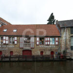 Canal-side façade photograph of the Ark Van Zarren shop in Bruges, capturing the historic building reflected in the water and integrated into the picturesque canal scenery, ideal for décor and travel‑oriented photo licensing without promoting any specific products.