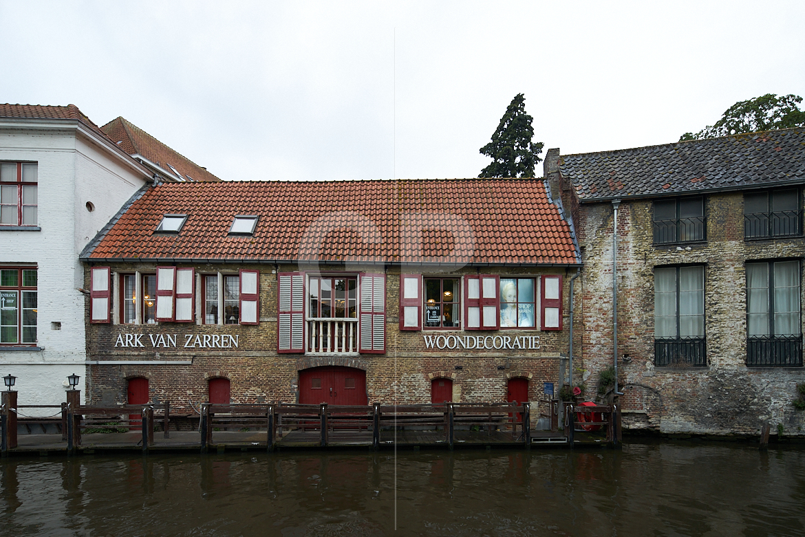 Canal-side façade photograph of the Ark Van Zarren shop in Bruges, capturing the historic building reflected in the water and integrated into the picturesque canal scenery, ideal for décor and travel‑oriented photo licensing without promoting any specific products. Canal-side façade photograph of the Ark Van Zarren shop in Bruges, capturing the historic building reflected in the water and integrated into the picturesque canal scenery, ideal for décor and travel‑oriented photo licensing without promoting any specific products.